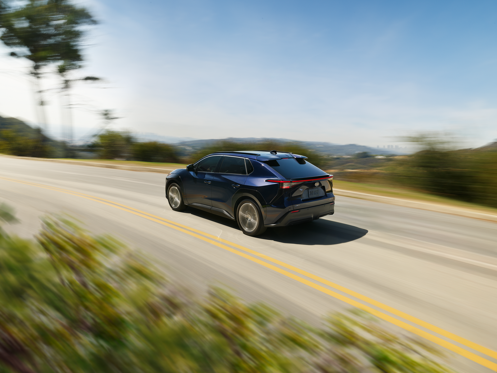 Blue Toyota bZ driving on a hillside road, rear three-quarter view