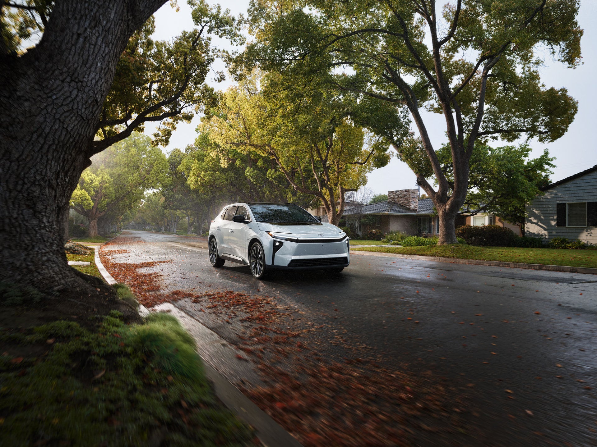 A white Toyota bZ parked on a wet residential street lined with trees