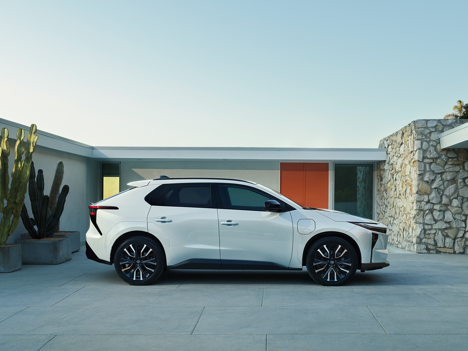 Side view of a white Toyota bZ outside a modern house