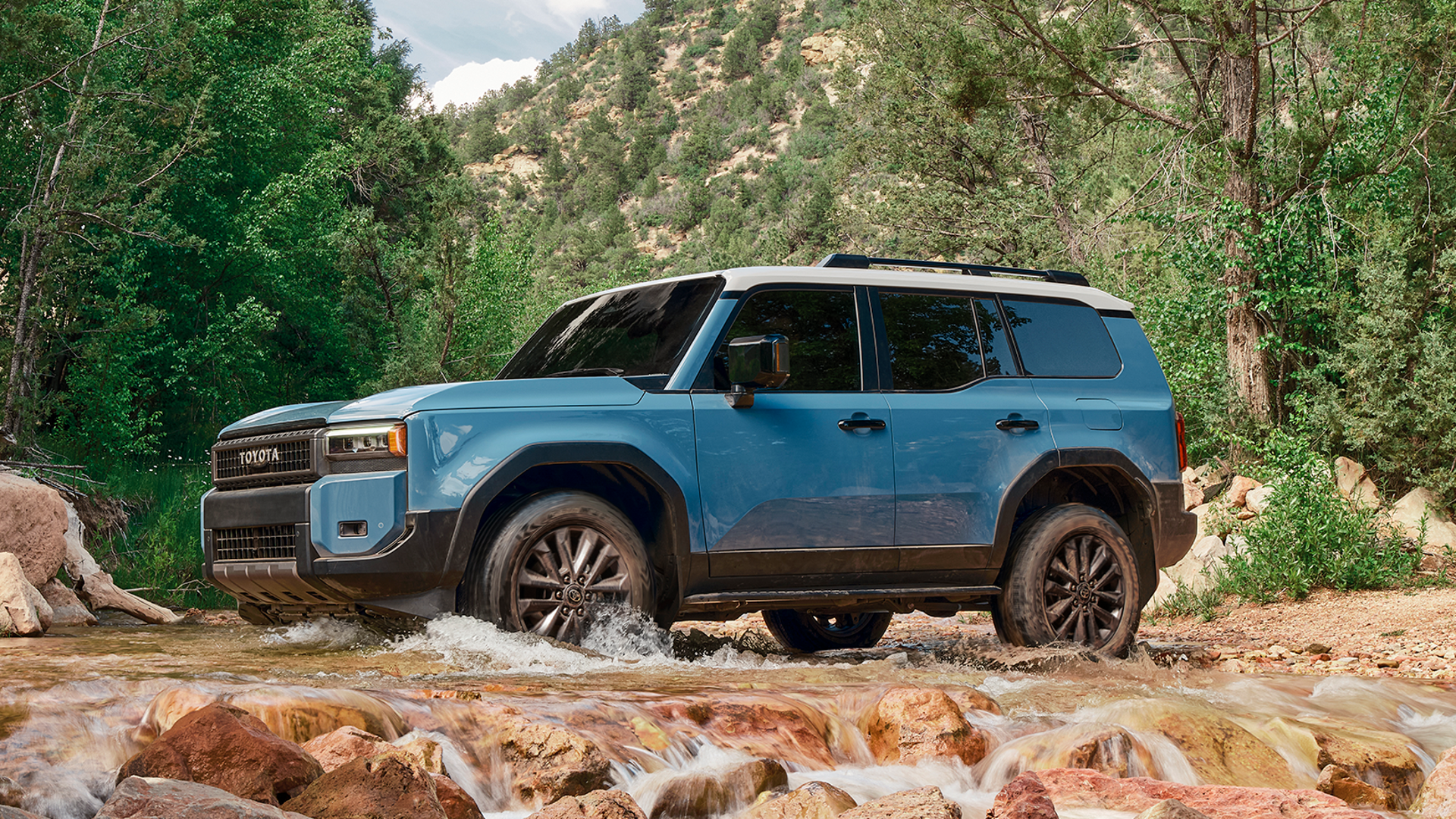 Blue Toyota Land Cruiser driving through a shallow rocky creek