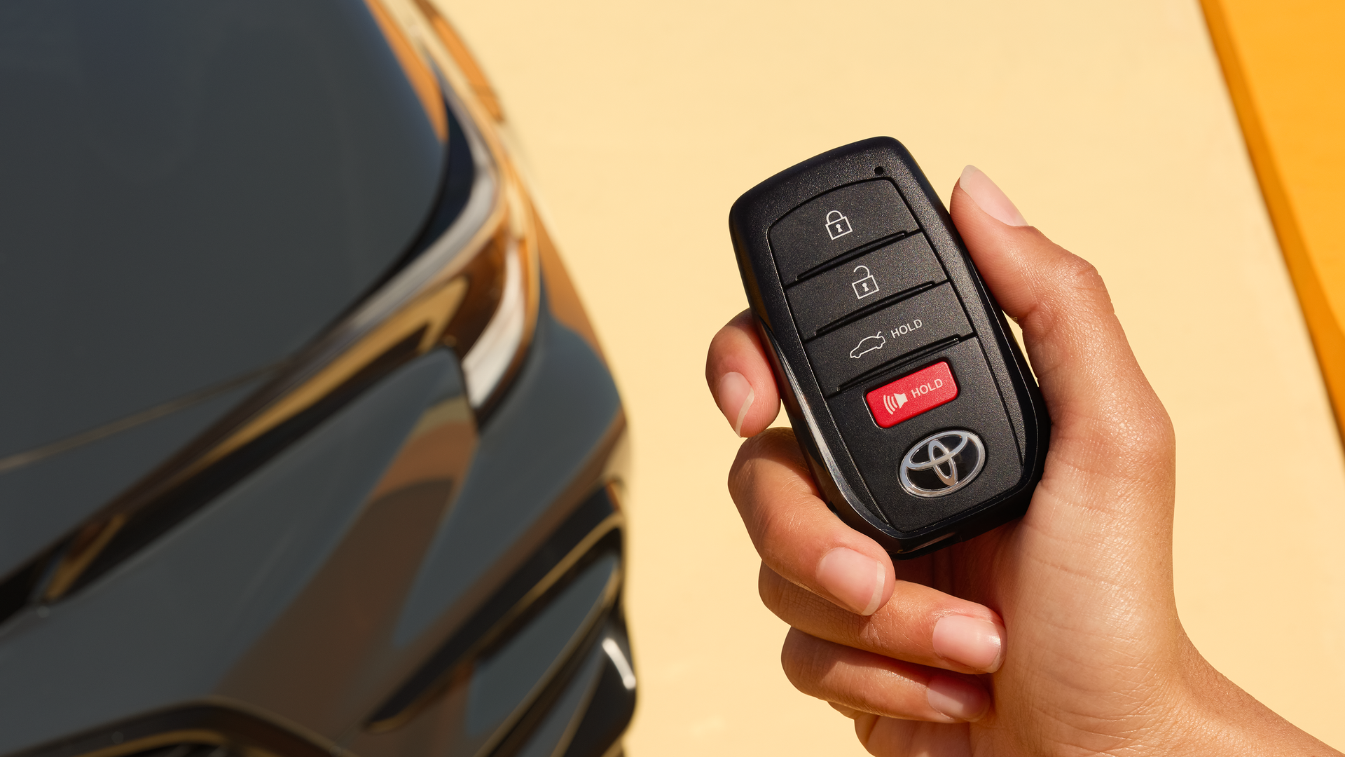 Hand holding a Toyota smart key next to a Corolla