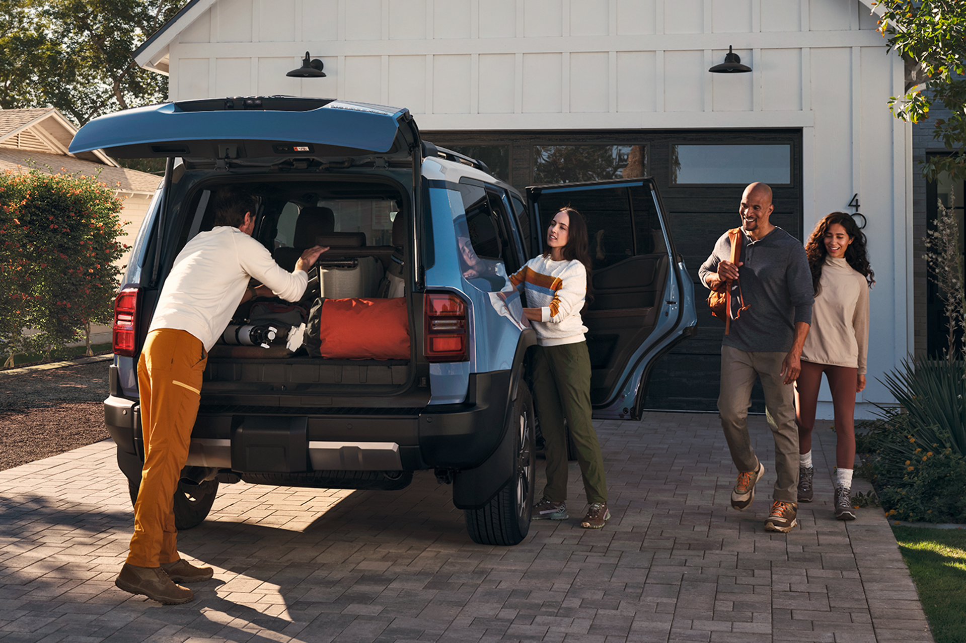 Family loading the cargo area of a blue Toyota Land Cruiser in a driveway