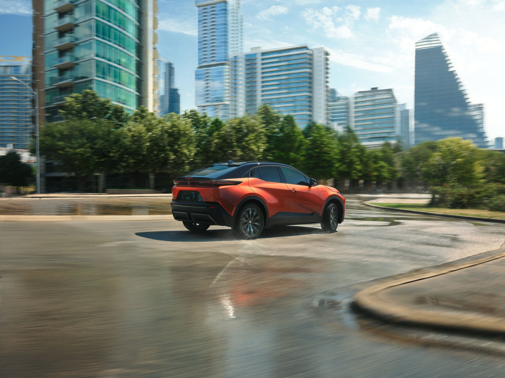 An orange Toyota C-HR electric SUV driving through a city plaza